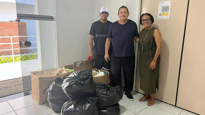 Todas as Notícias 4 Fotografia com a presença de 3 pessoas, 2 homens e 1 mulher; a frente deles algumas caixas e sacolas pretas.