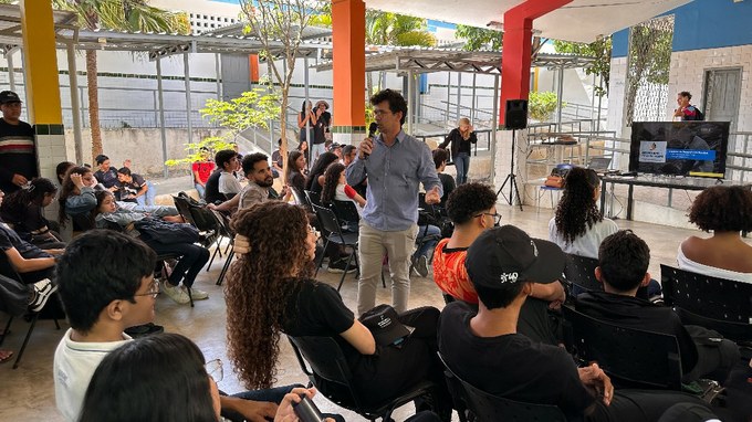 Projeto educativo de enfrentamento ao trabalho escravo contemporâneo chega à ECIT Escritor Virginius da Gama e Melo, em Campina Grande - CSJT2 13 Fotografia com a presença de um homem com microfone na mão e algumas pessoas ao lado sentadas.