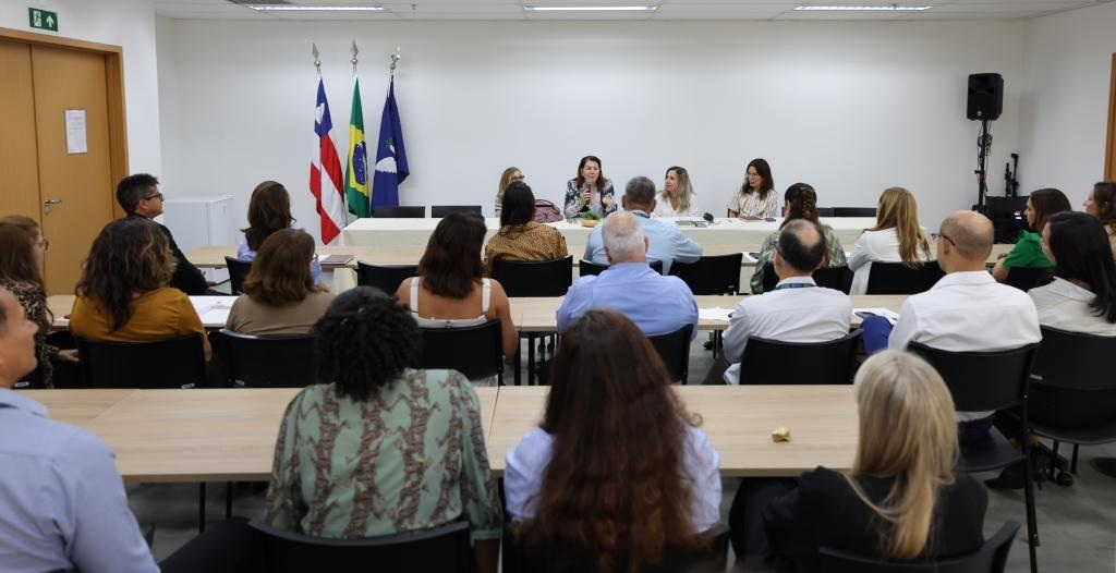 Fotografia com diversas pessoas sentadas e uma delas está com um microfone.